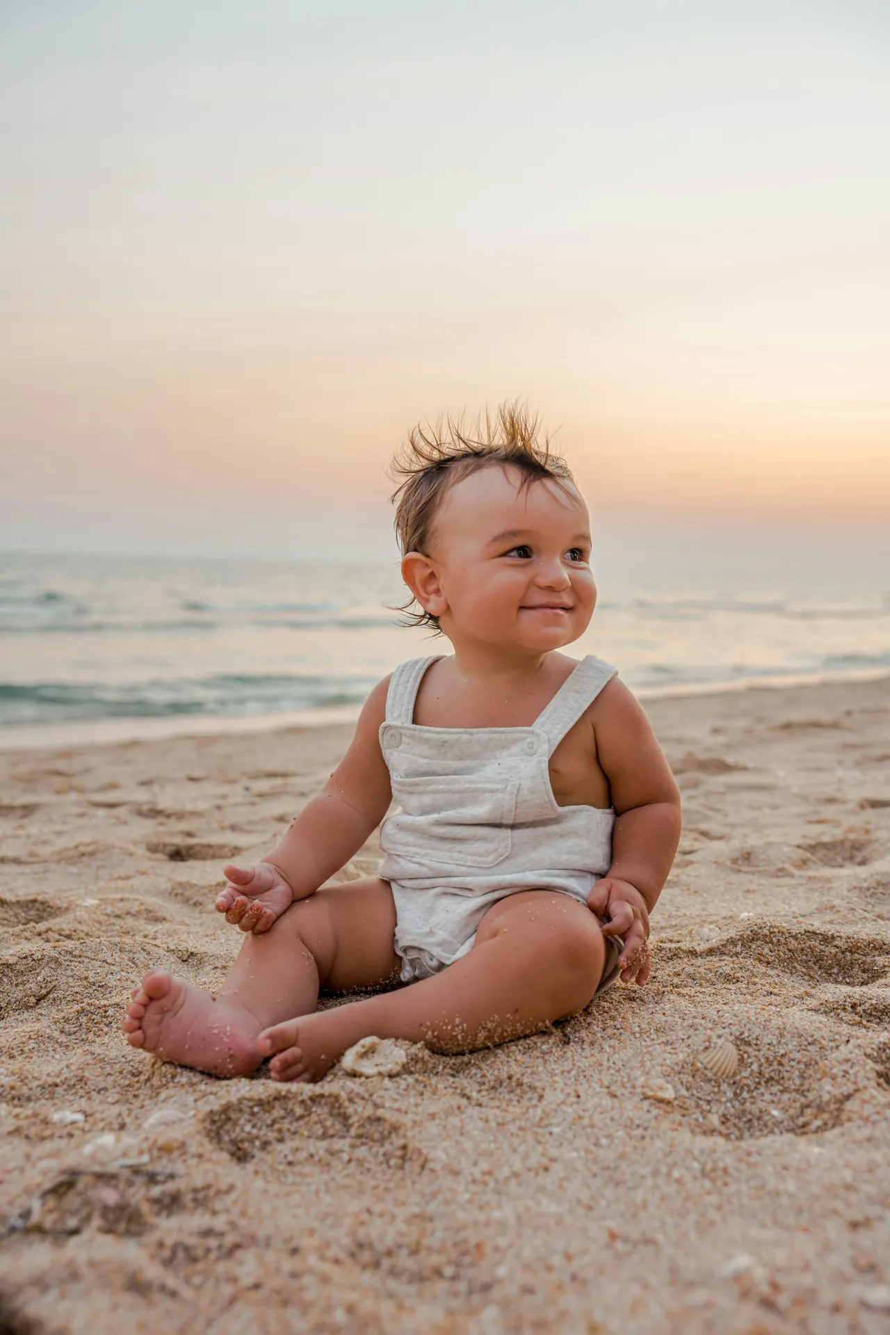 Toddler sitting in the sand on a beach at sunset