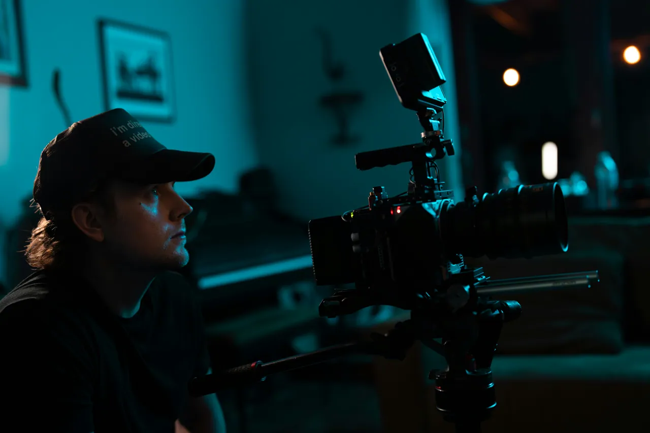 Beau Horyza in a dark, teal-lit room, lining up a shot on a cinema camera
