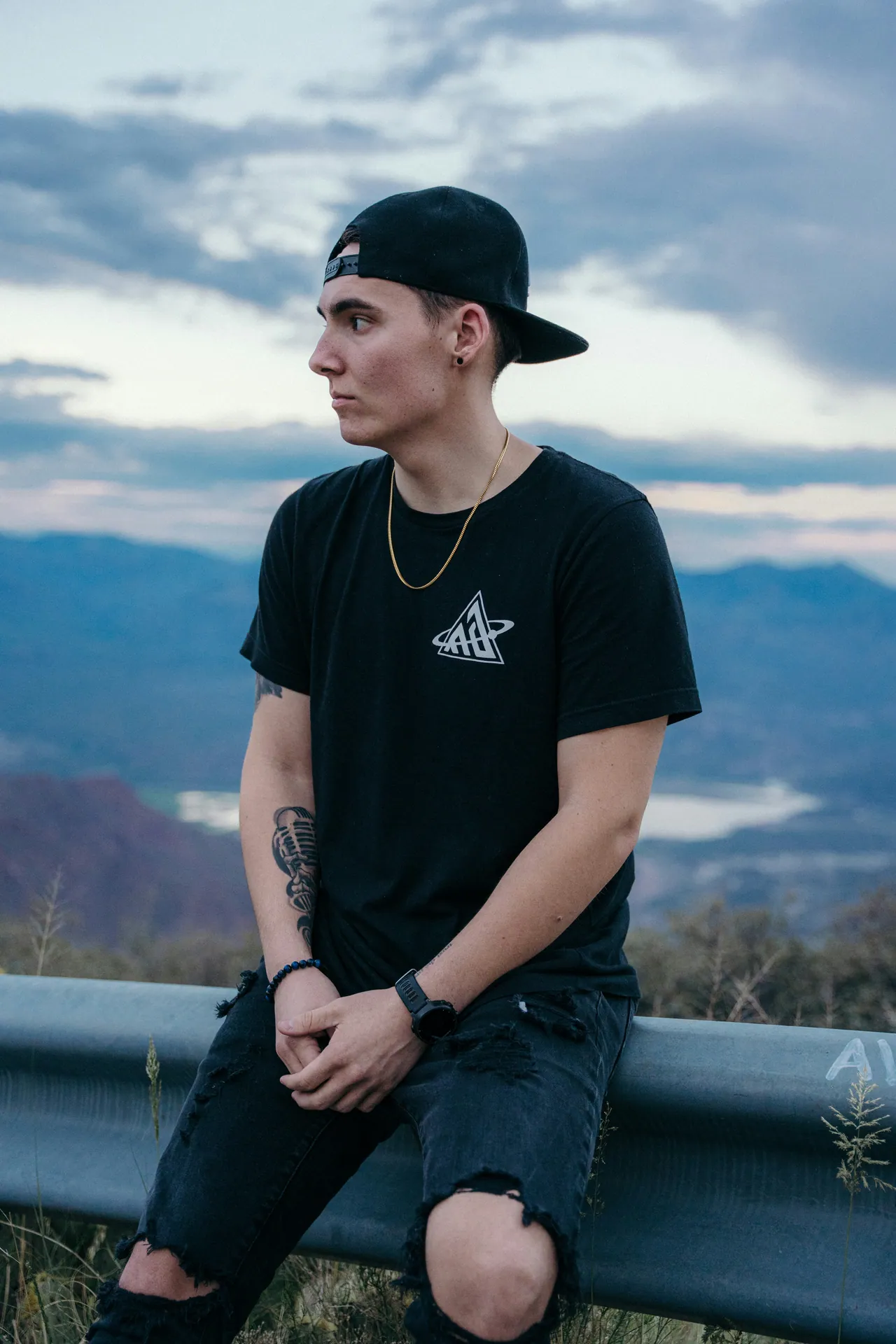 Man in a cap sitting on a guardrail above a lake