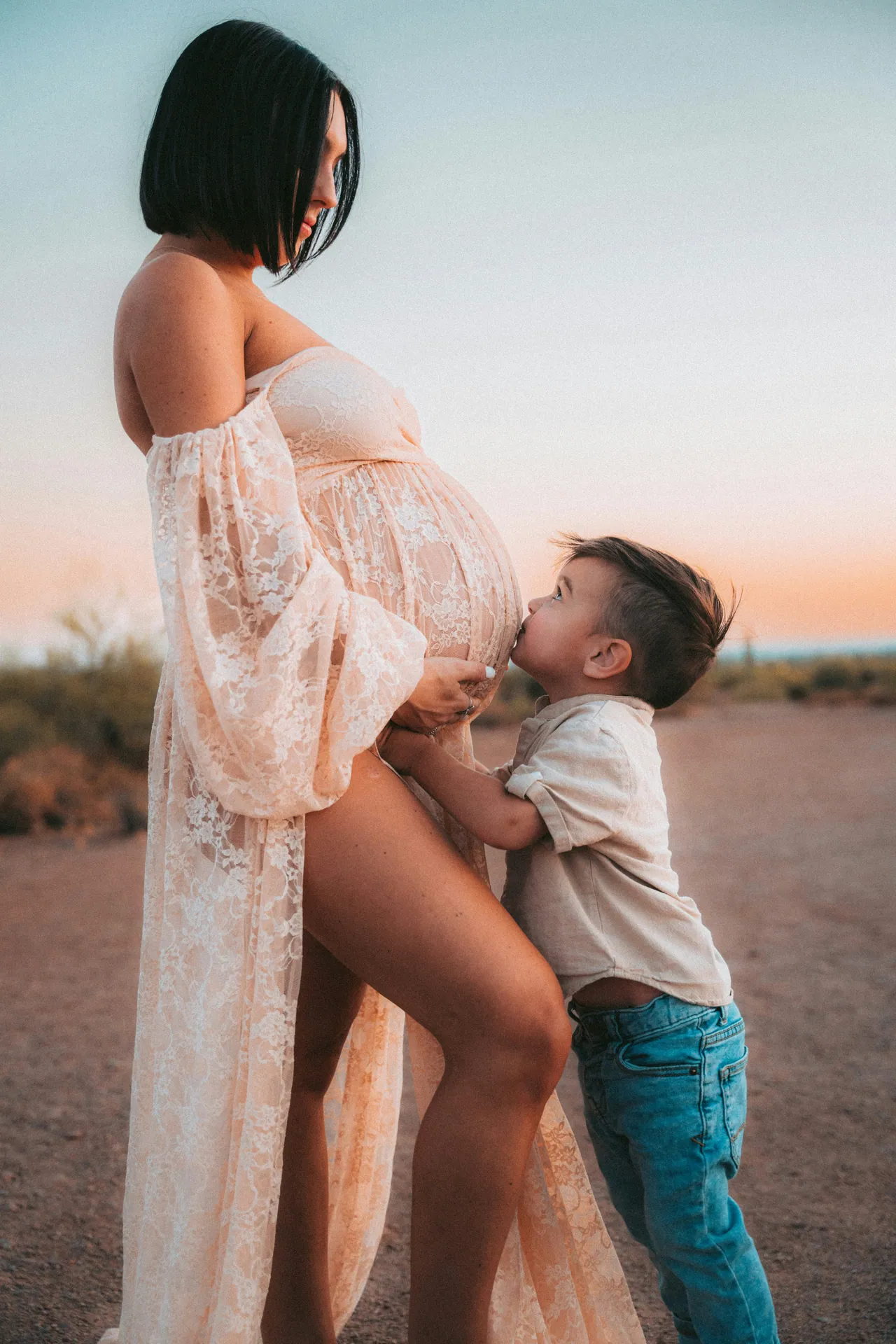 Mother in a lace gown kissed by her son in the desert at dusk
