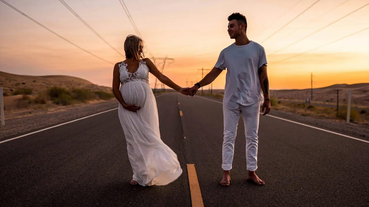 Expectant couple holding hands on an empty desert road at sunset